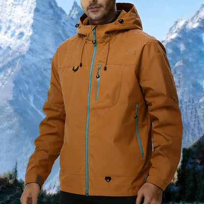 Veste softshell imperméable coloris caramel/ambre face — capuche, zips bleu-vert, fond montagne enneigée