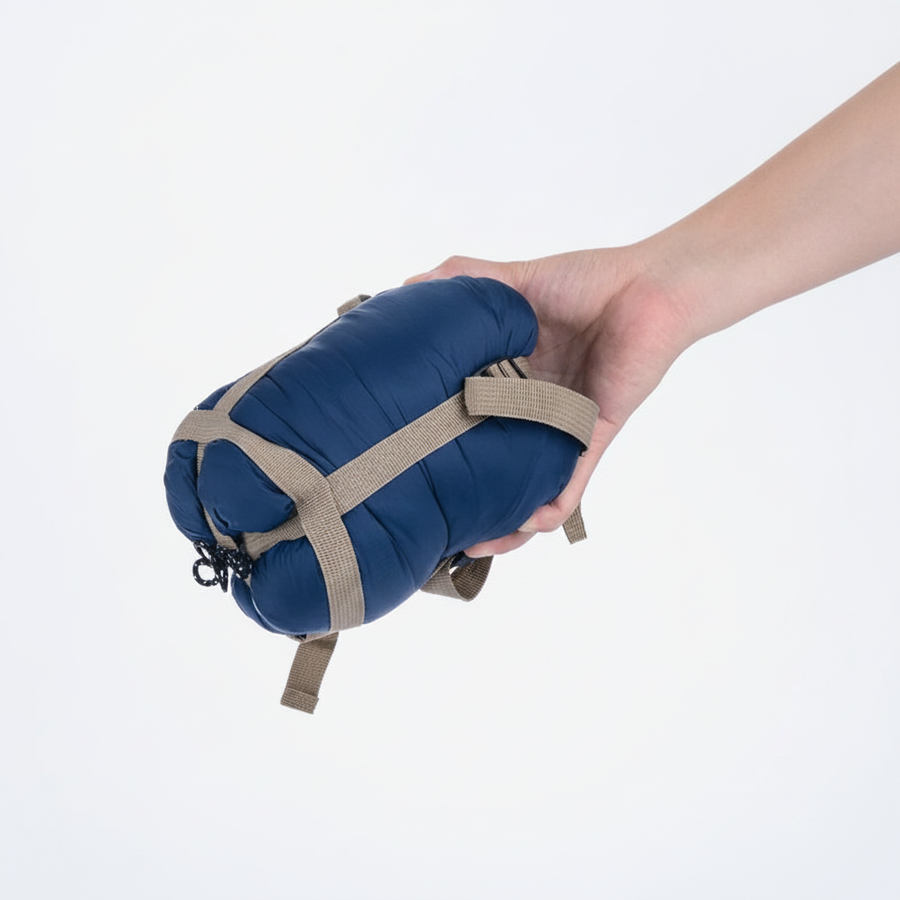 Sac de couchage Velotrip compressé et sanglé, tenu en main — vue studio